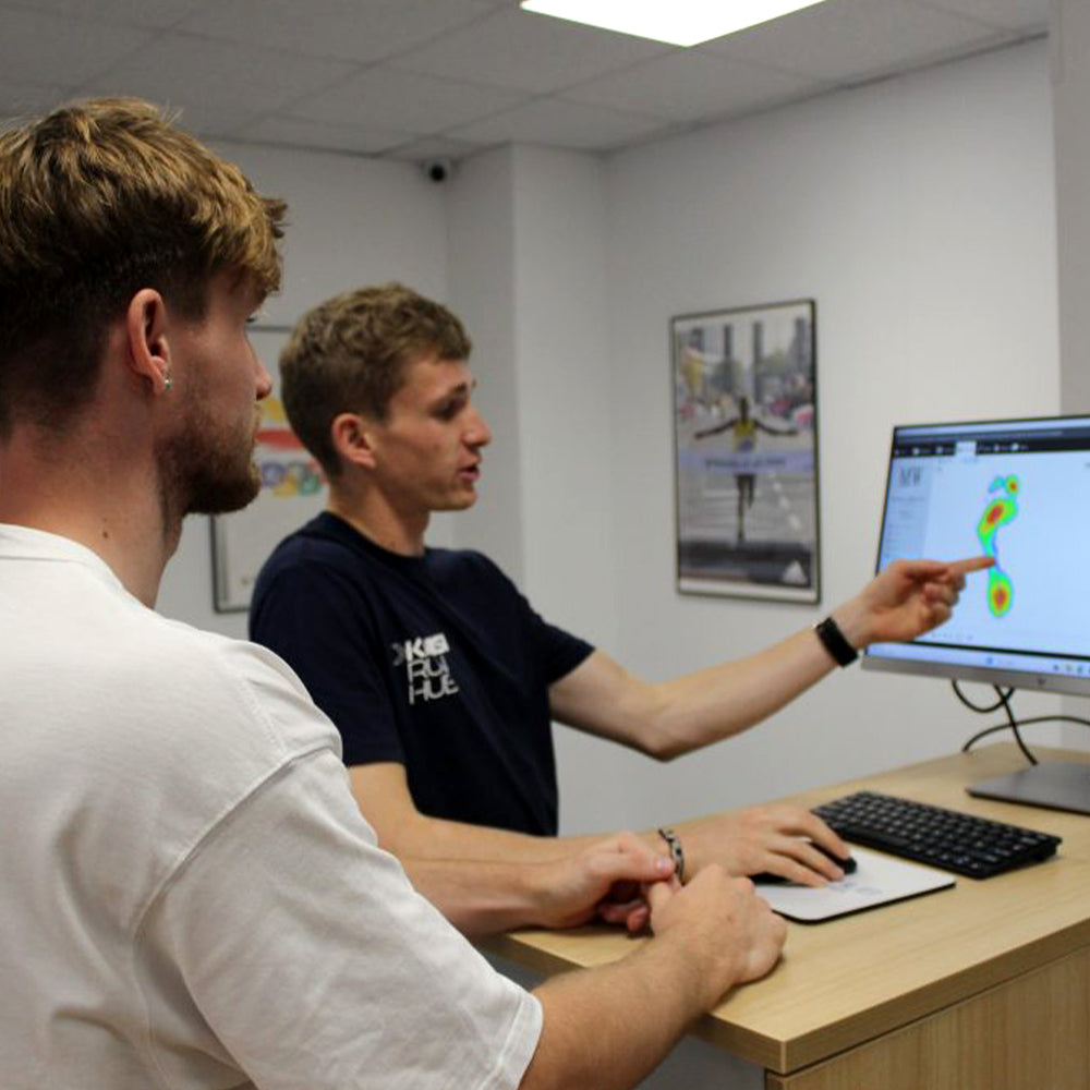 Image of Jamie from the Kinisi Run-Hub at a computer showing a customer an on-screen foot heat-map as part of movement analysis
