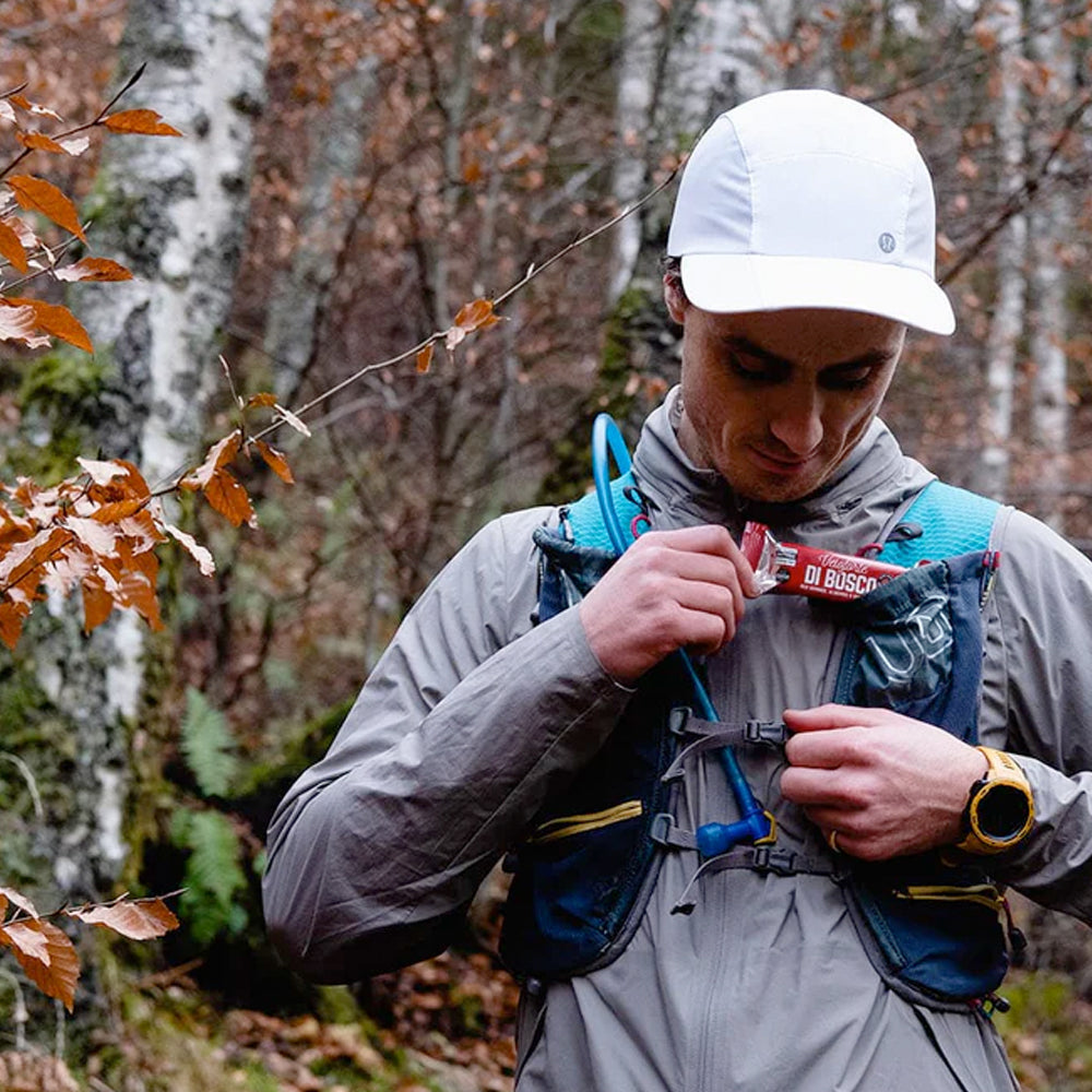 Image of a man standing amongst some trees wearing running gear while taking a nutition bar out of a running vest