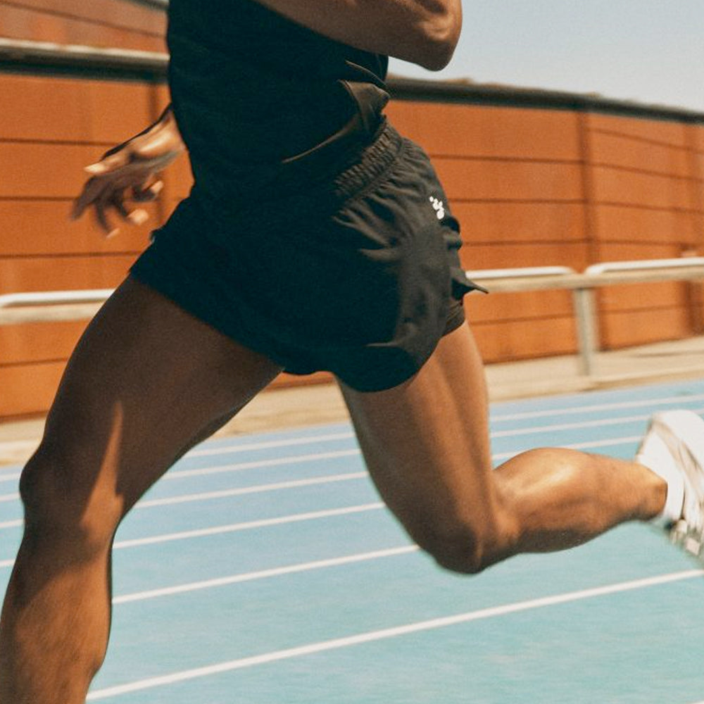 Photograph of the lower half of a persons body running on a racing track while wearing running shorts