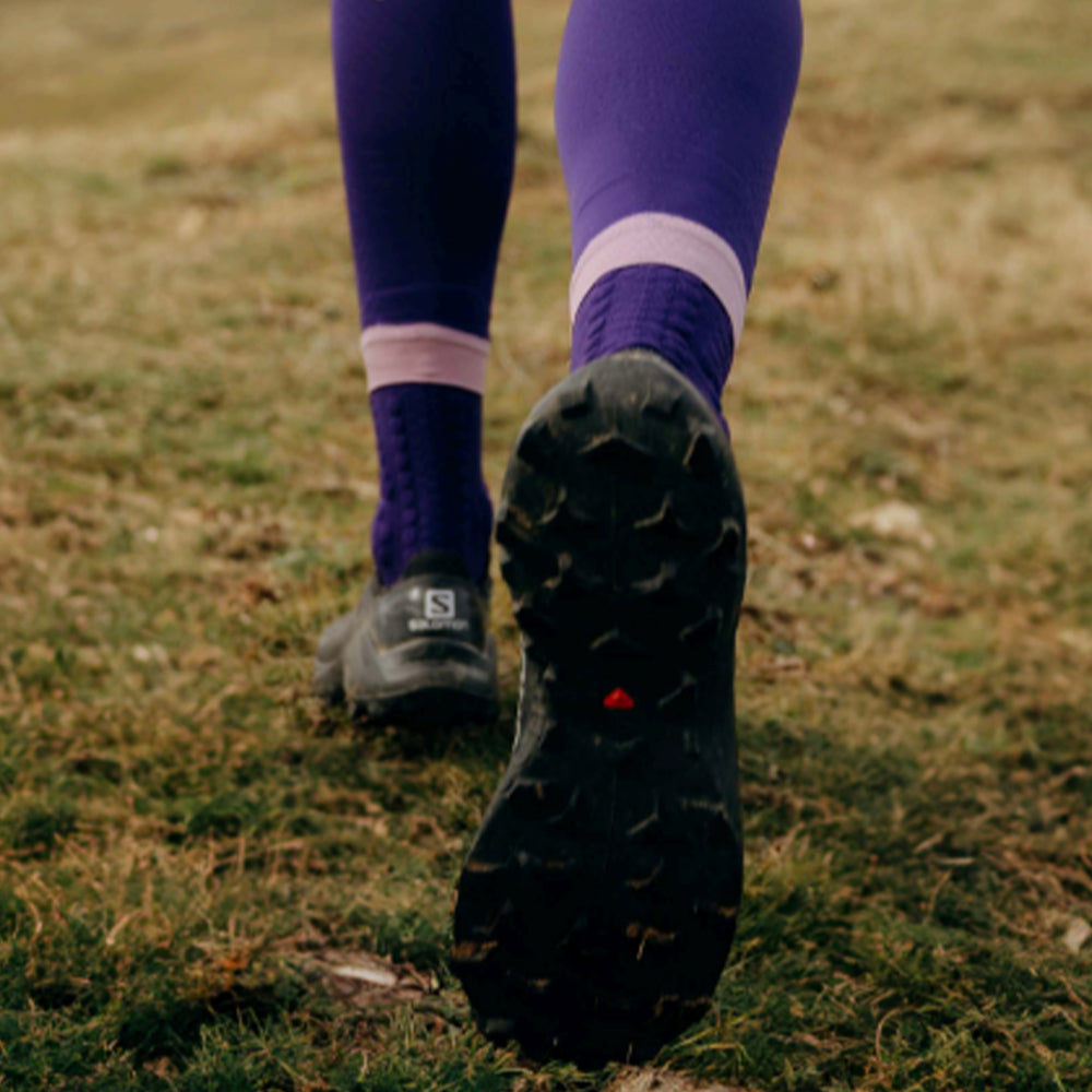 Image of a person's legs as they run through a field wearing compression socks and running trainers