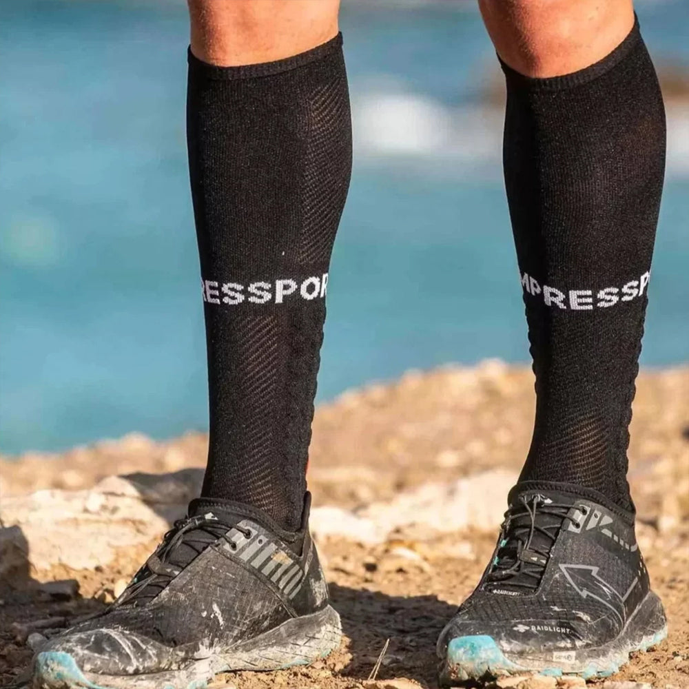 Image of the lower half of a persons legs stood on a muddy ground wearing running trainers and compression socks