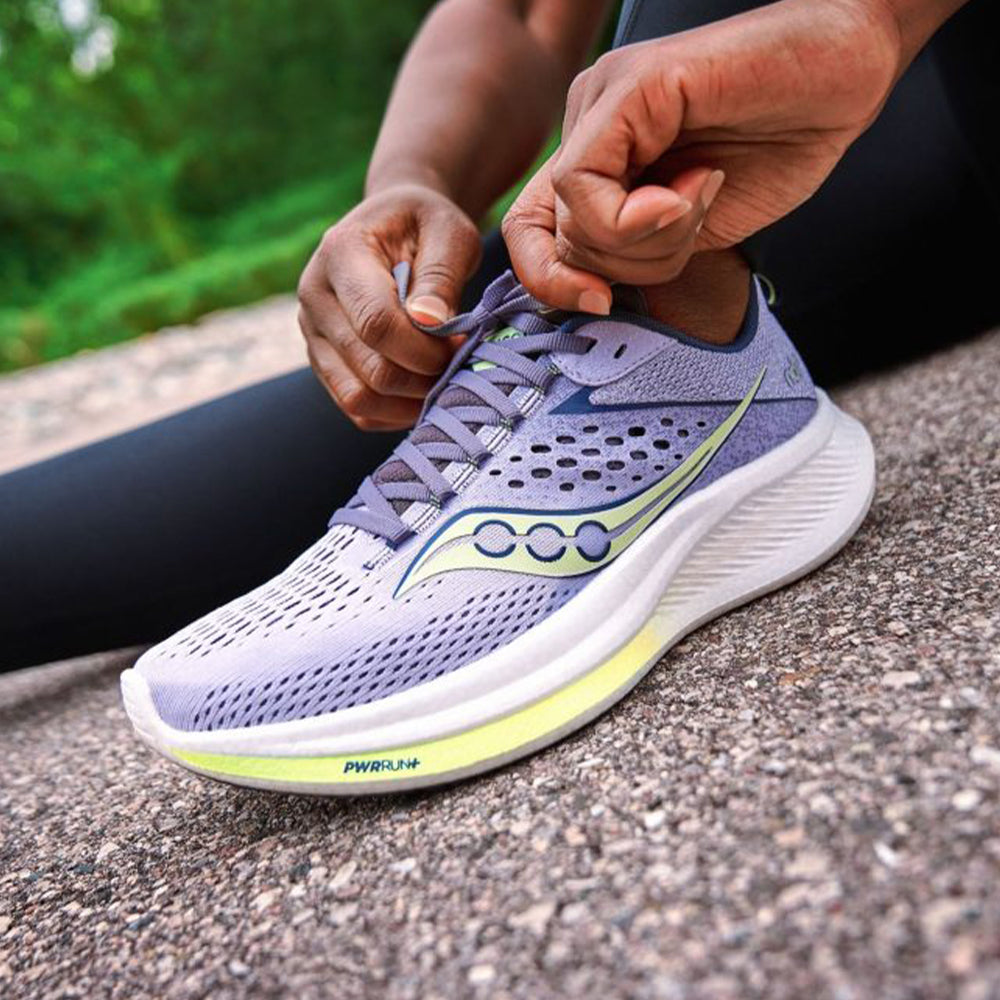 Photograph of hands tying laces on a pair of light purple Saucony running shoes
