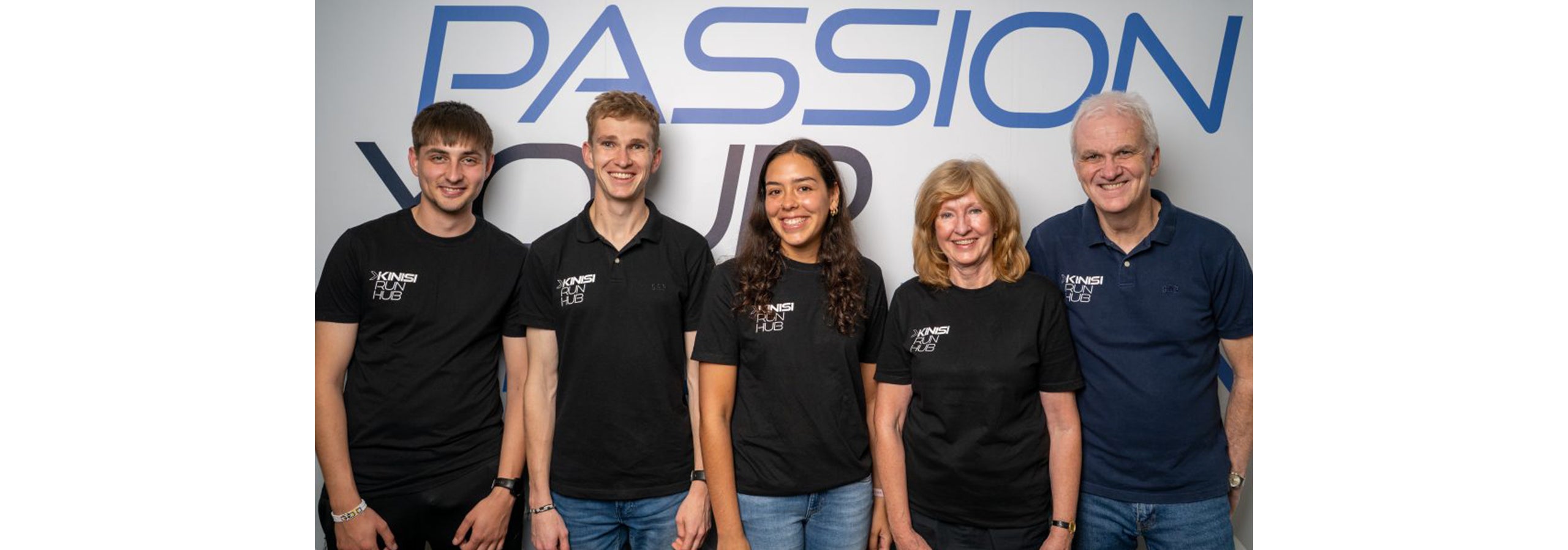 A photograph of the Kinisi Run Hub team stood in front of a sign in the Kinisi font reading 'passion'