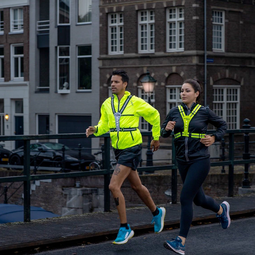 Photograph of a man and woman running together in a city street while wearing hi-vis running gear