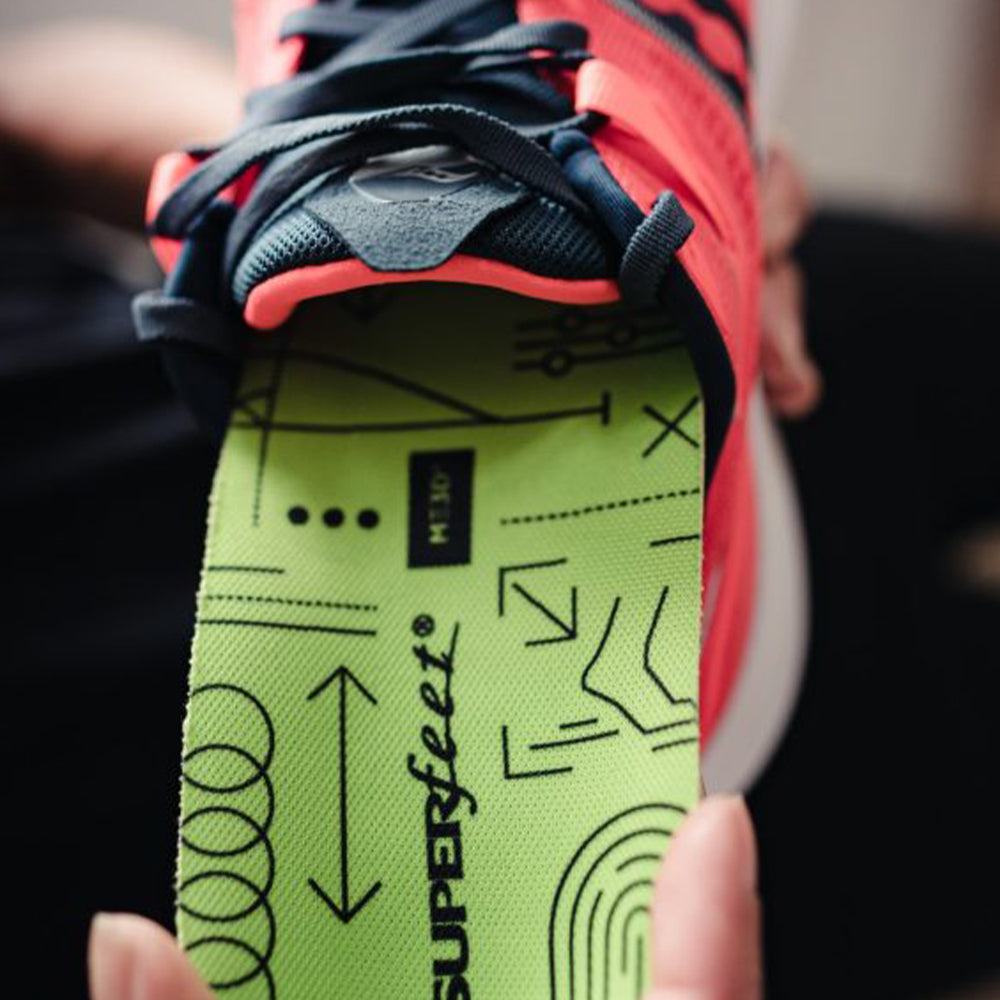 Image of a hand inserting a Superfeet insole into a pair of red running shoes