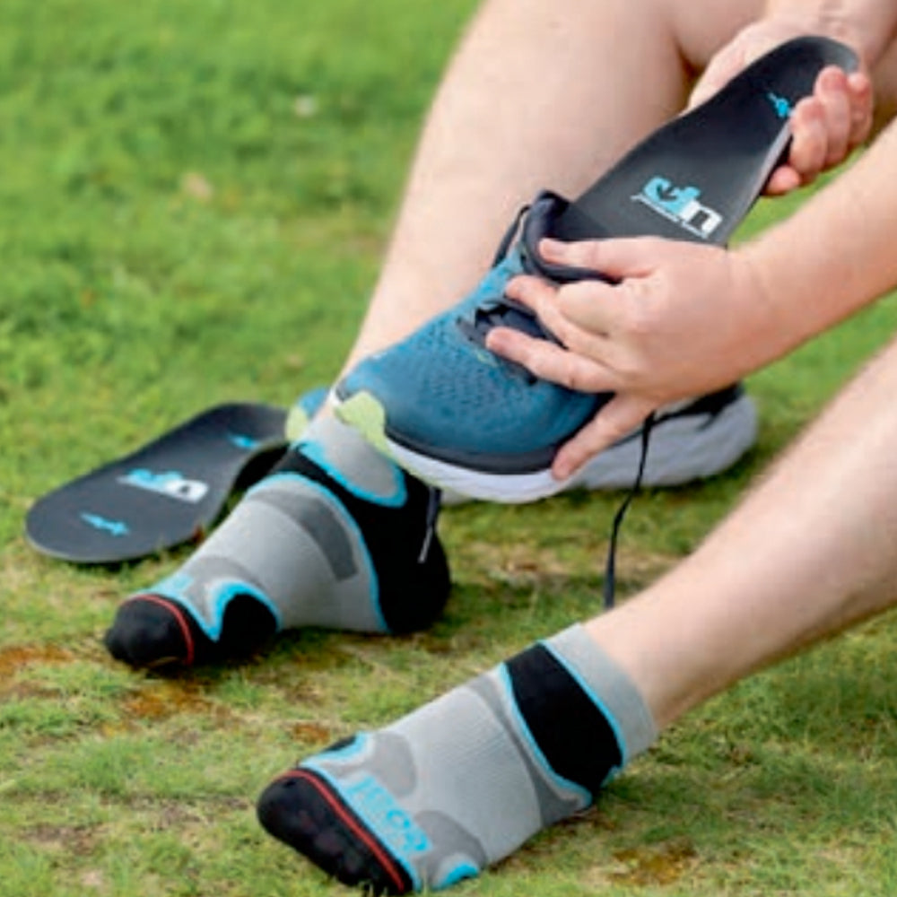Image of someone sitting on grass fitting Up branded insoles into a running shoe