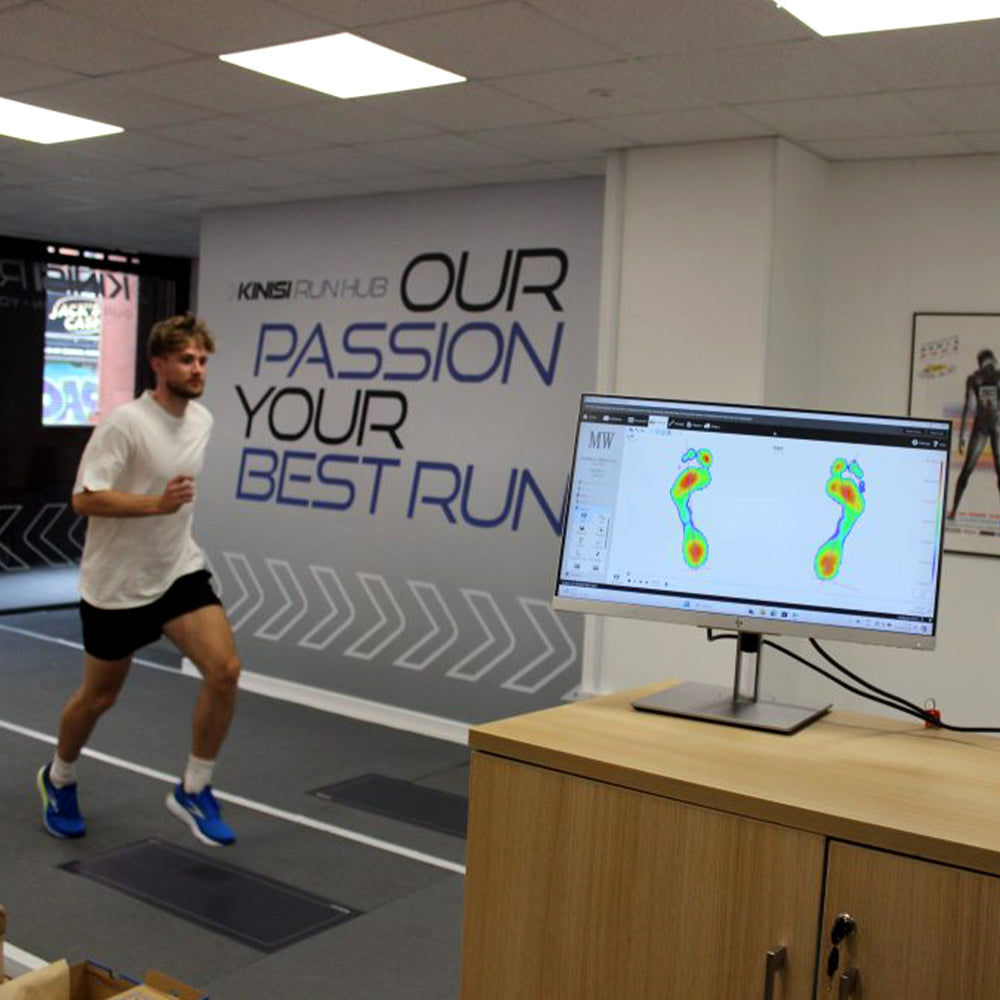 Image of a customer running on an indoor analysis track at the Kinisi Run-Hub, with a computer showing an on-screen foot heat-map as part of movement analysis