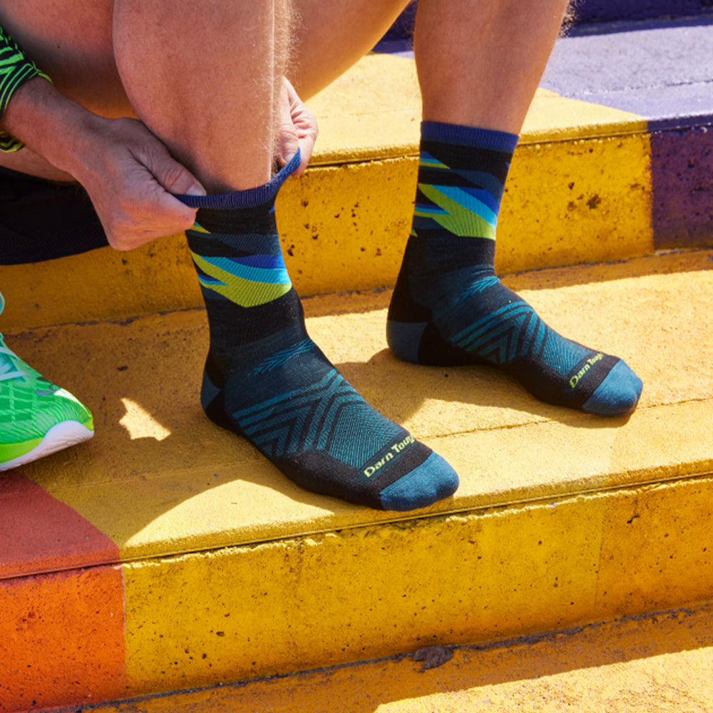 Image of a man sat on stairs outside pulling on a running sock